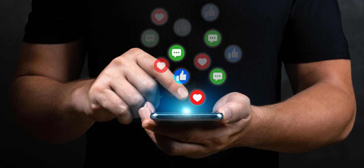 Hands holding a phone with chat, like and heart notifications floating up from the screen