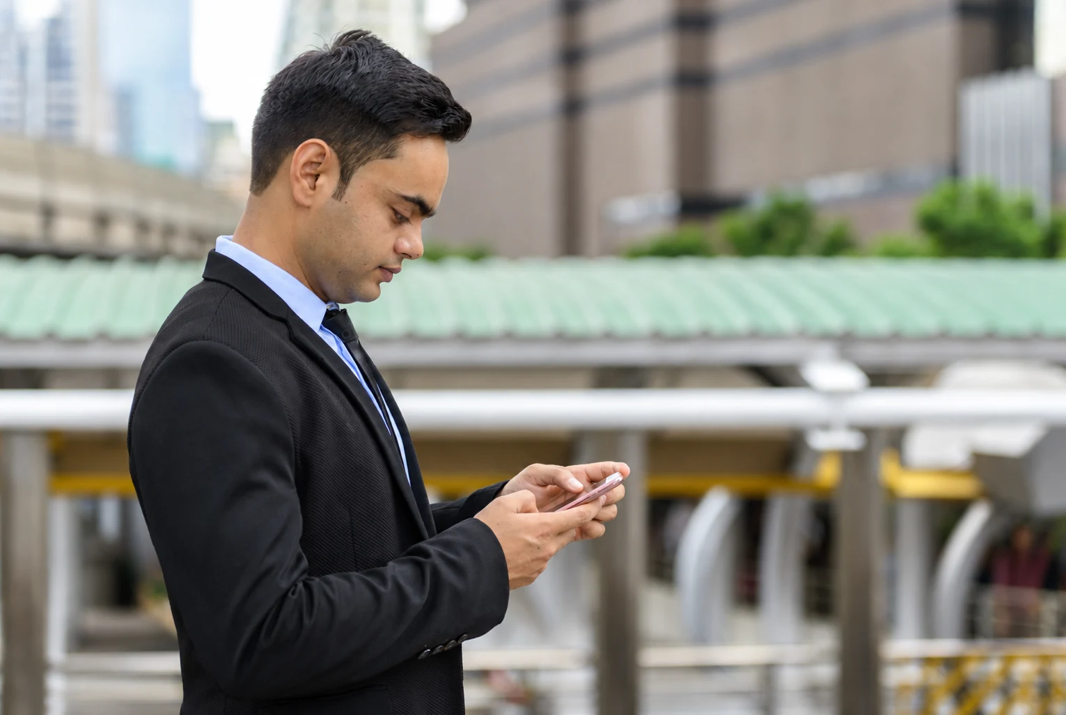 A man in a suit reading messages on a phone outdoors