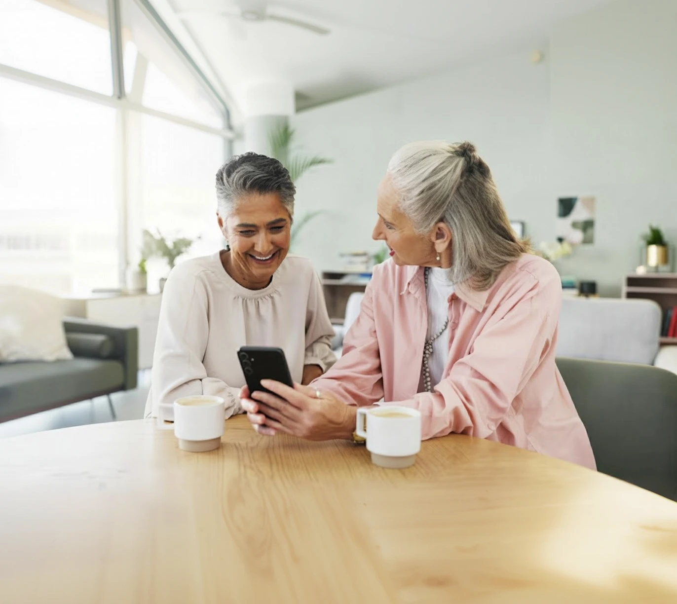 Two friends laughing over a phone at a café table